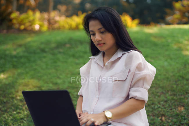 Молода азіатська жінка використовує ноутбук у парку — стокове фото