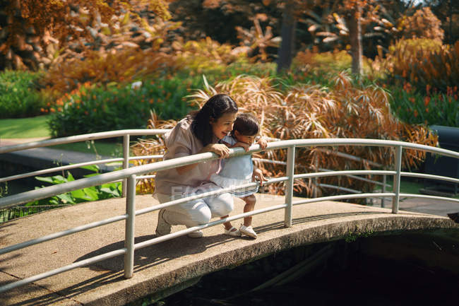 Lindo asiático madre y hija buscando fuera de barandilla en parque - foto de stock