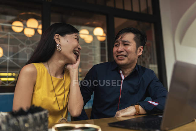 Счастливая молодая азиатская пара с ноутбуком в кафе — стоковое фото