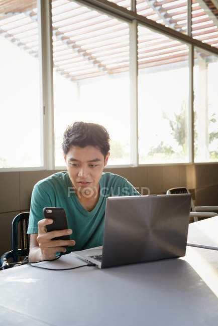 Jovem atraente asiático homem usando smartphone e laptop no café — Fotografia de Stock