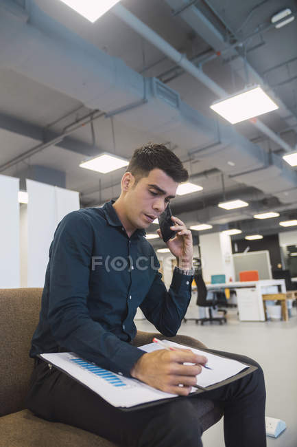Jovem asiático homem de negócios falando no smartphone no escritório moderno — Fotografia de Stock
