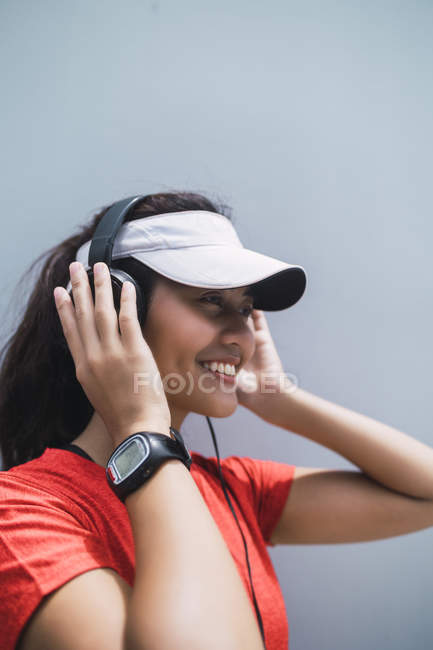 Jovem asiático mulher esportiva usando fones de ouvido contra fundo cinza — Fotografia de Stock