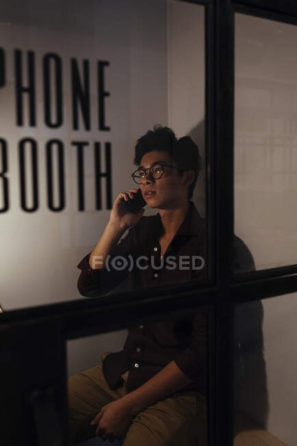 Asian man with glasses on talking mobile phone in office — Stock Photo