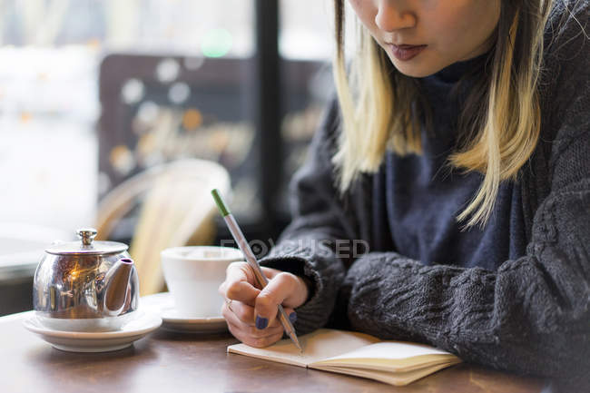 Young attractive casual asian woman writing notes in cafe — Stock Photo