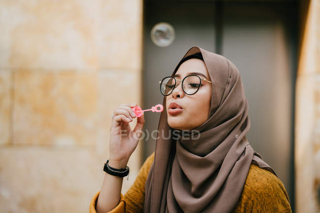Jovem asiático muçulmano mulher no hijab fazendo bolhas no rua — Fotografia de Stock