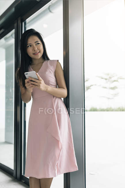 Молода азіатська успішна бізнес-леді зі смартфоном в сучасному офісі — стокове фото
