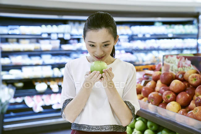 Улыбающаяся азиатка держит яблоко на рынке — стоковое фото