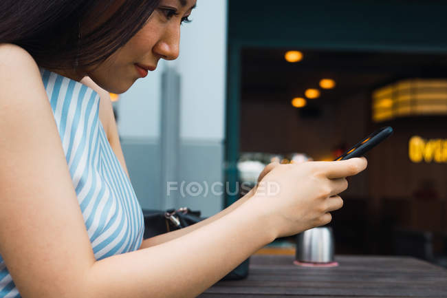 Vista lateral de jovem mulher asiática com smartphone — Fotografia de Stock