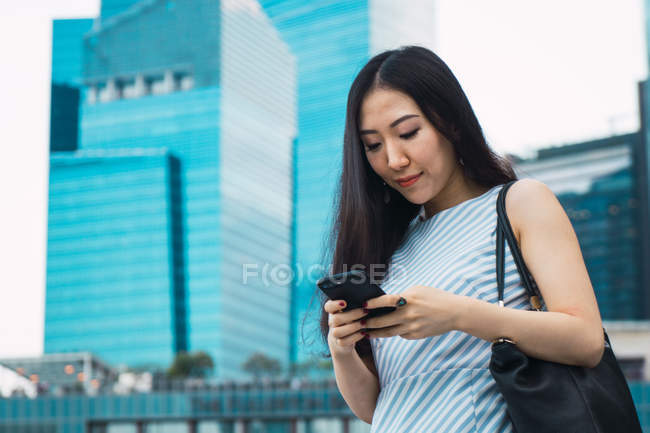 Junge Asiatin fährt mit Smartphone gegen Hochhäuser — Stockfoto