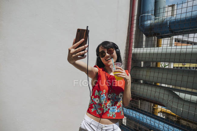 Asian woman with headphones and drink — Stock Photo