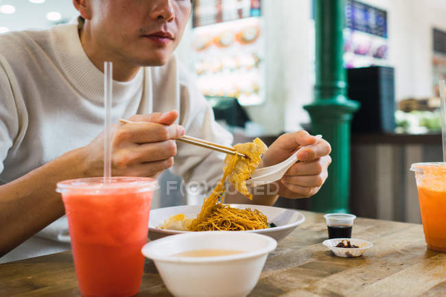 Asiático hombre comer comida con palillos en café - foto de stock