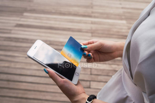 Imagem cortada de mulher segurando cartão de crédito e smartphone — Fotografia de Stock