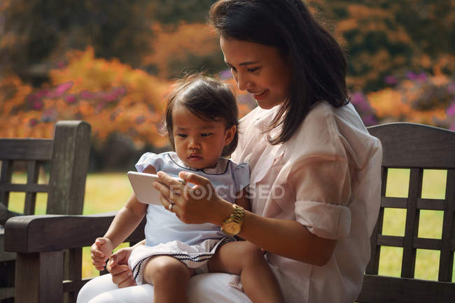Cute asian mother and daughter using smartphone in park — Stock Photo