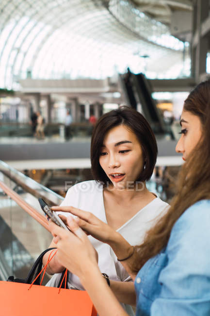 Молодые красивые азиатские женщины, смотрящие на смартфон в торговом центре — стоковое фото