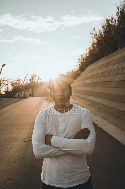 Young Asian man standing against sunset with arms crossed — Stock Photo