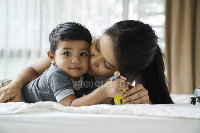 Madre e hijo jugando con juguetes en la cama - foto de stock