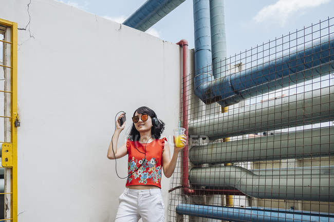 Азиатка в наушниках, стоящая у стены — стоковое фото