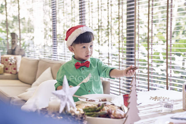 Glücklich junge asiatische Junge in Weihnachtsmann-Hut feiert Weihnachten am Tisch — Stockfoto