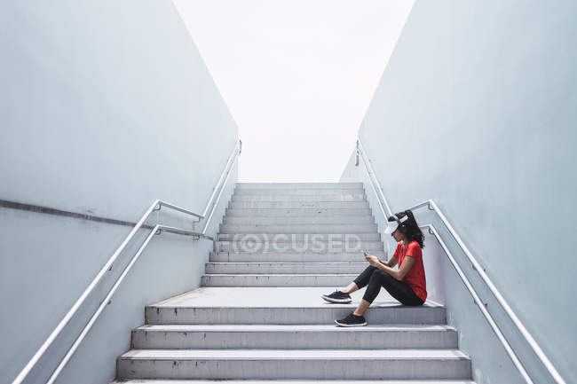 Seitenansicht einer jungen asiatischen sportlichen Frau mit Kopfhörern und Smart auf der Treppe — Stockfoto