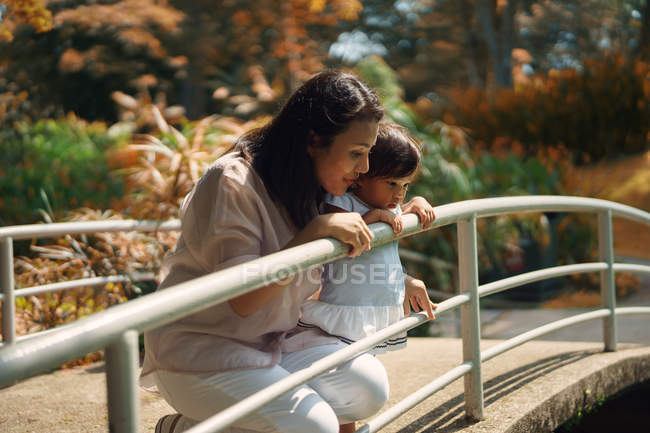 Cute asian mother and daughter looking out of railing in park — Stock Photo
