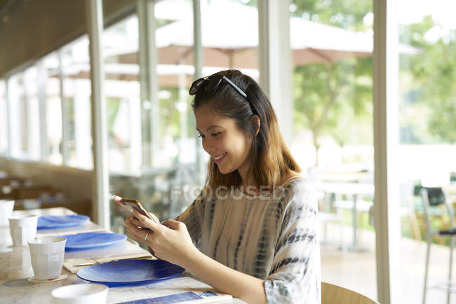 Junge hübsche asiatische Frau mit Smartphone im Café — Stockfoto