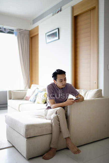 Зрелый азиатский случайный человек, использующий смартфон дома — стоковое фото