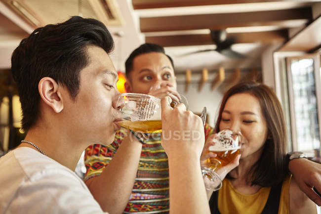 Молоді азіатські друзі п'ють пиво разом у барі — стокове фото
