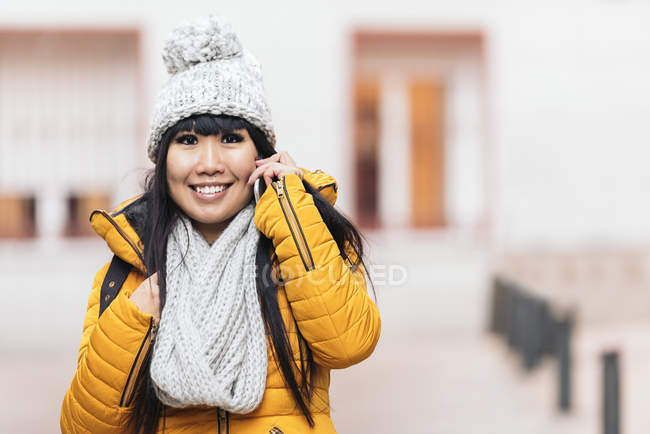 Молода приваблива азіатська жінка говорить на смартфоні на вулиці — стокове фото