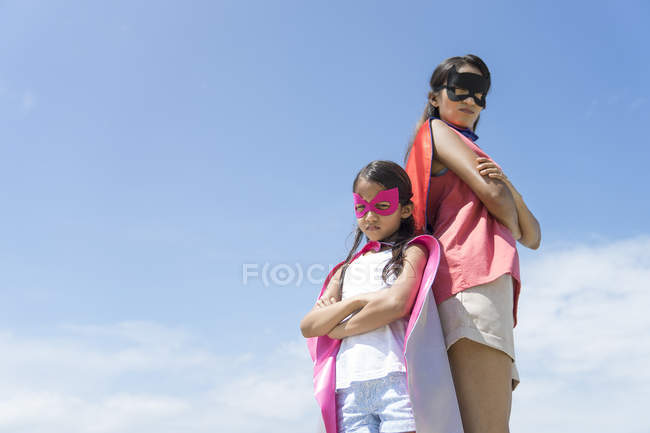 Giovane madre asiatica con carina figlia in costumi da supereroe in posa contro il cielo blu — Foto stock