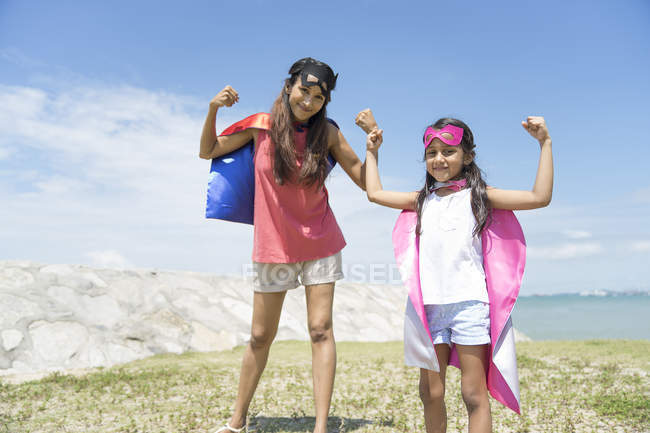 Jeune mère asiatique avec fille mignonne en costumes de super-héros posant contre le ciel bleu — Photo de stock