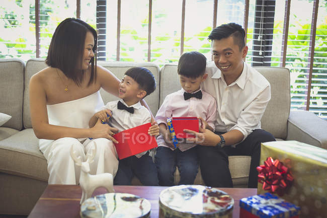 Family of four sits on the sofa and opens Christmas presents — Stock Photo