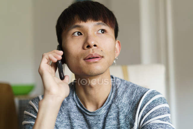 Молодой взрослый азиат мужчина, использующий смартфон дома — стоковое фото