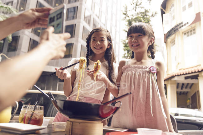 Feliz asiático familia comer fideos juntos en calle café y tomando foto - foto de stock