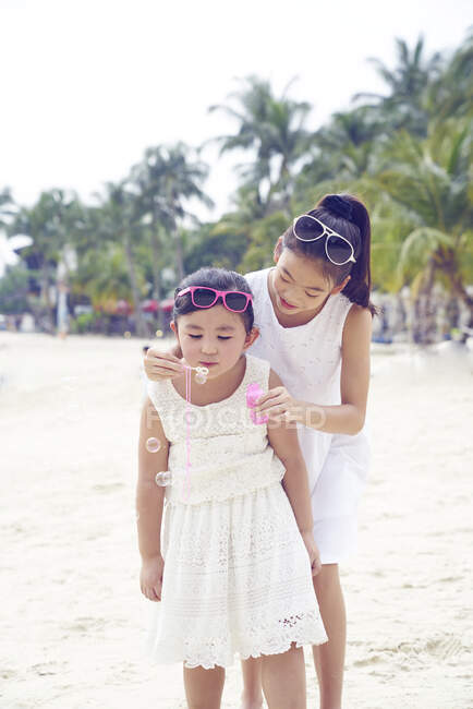 RELEASES Two little sisters spending time together on beach and blowing bubbles — Stock Photo
