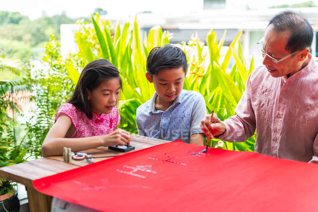 Happy asian family together, grandfather and grandchildren drawing hieroglyphs — Stock Photo