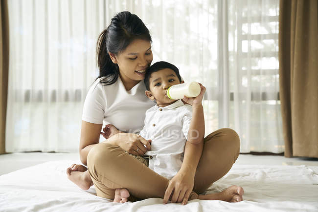 Ásia mãe relógios como ela filho alimenta no leite garrafa — Fotografia de Stock