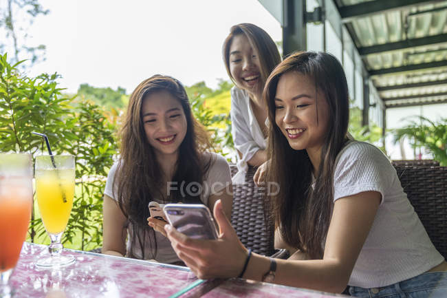 Drei asiatische Mädchen, die gemeinsam im Café auf das Smartphone schauen — Stockfoto