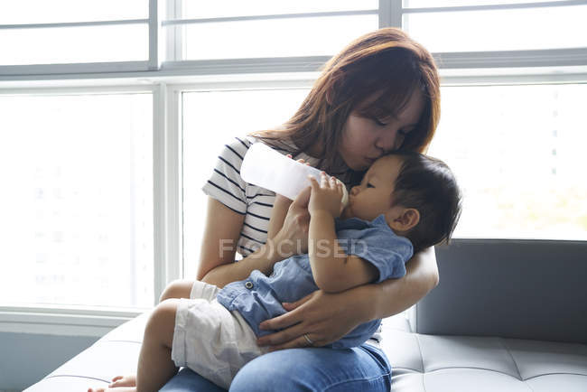Jovem mãe alimentando seu leite de bebê de uma mamadeira — Fotografia de Stock