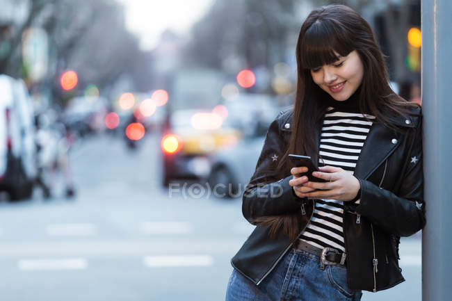 Jeune attrayant asiatique femme en ville en utilisant smartphone — Photo de stock
