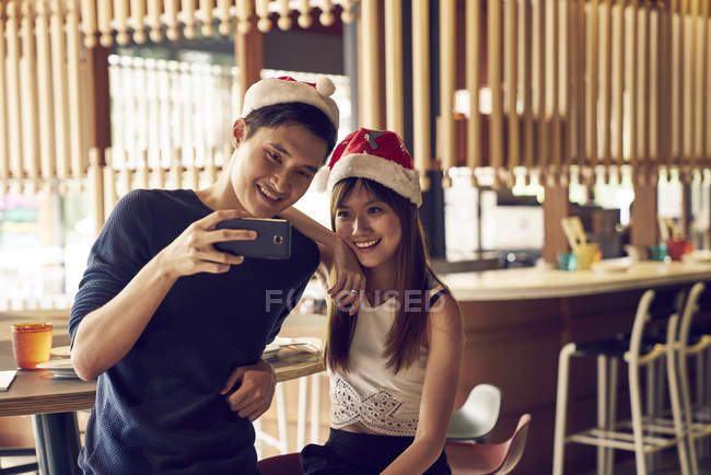 Feliz joven asiático amigos pareja navidad juntos en café y tomando selfie - foto de stock