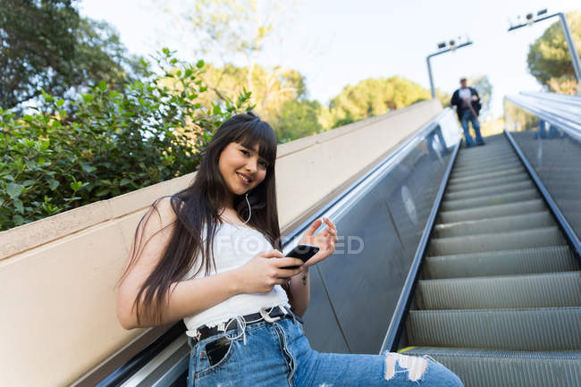 Eurasian woman listening to music on escalator — Stock Photo