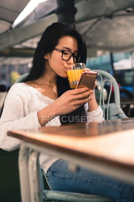 Femme chinoise avec téléphone et jus d'orange sur une terrasse de Madrid, Espagne — Photo de stock