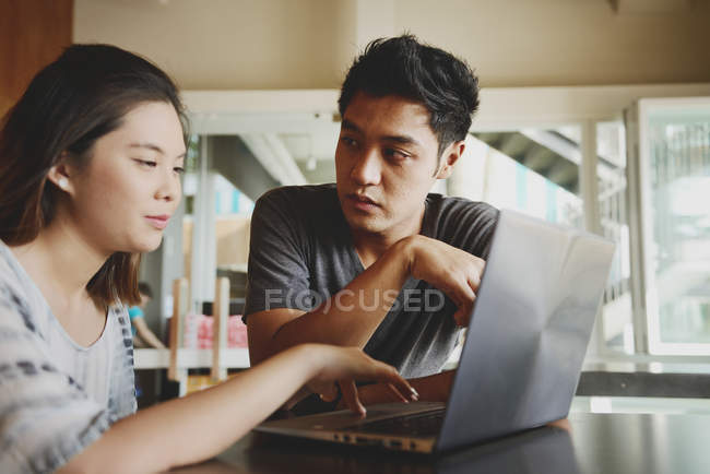 Young attractive asian couple using laptop in cafe — Stock Photo