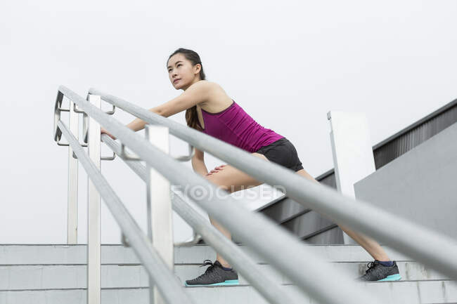 Uma jovem mulher asiática está se esticando em uma escada fora antes de sua corrida . — Fotografia de Stock