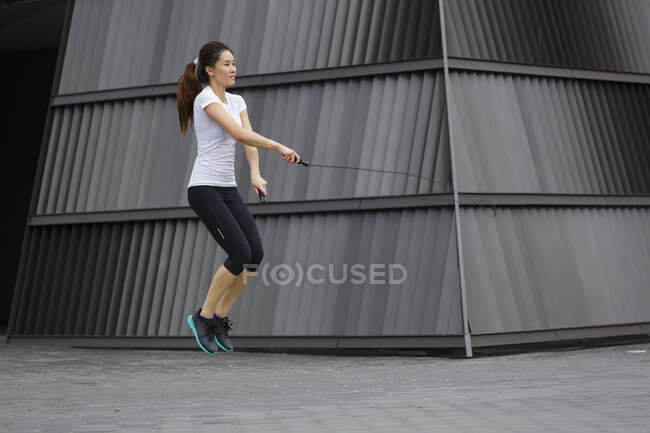 Una joven asiática está haciendo ejercicio con la cuerda saltando, al aire libre en Singapur . - foto de stock