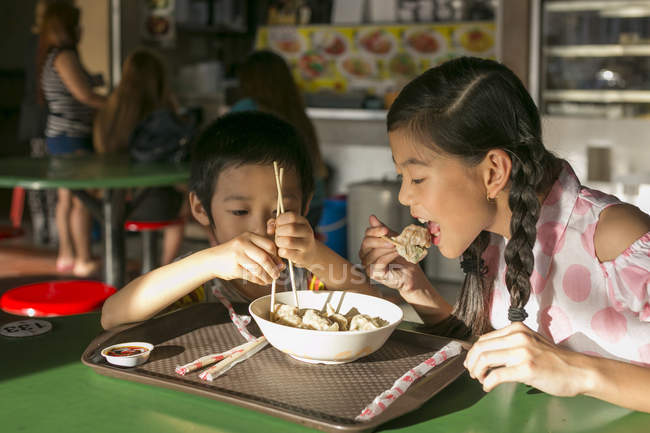 Two happy young asian children eating in cafe — Stock Photo