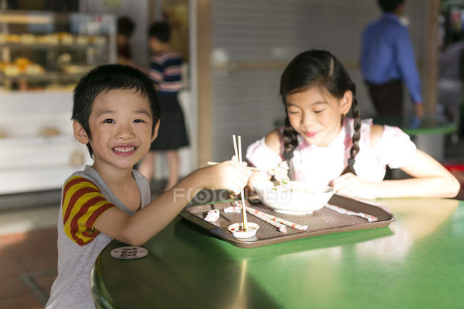 Deux heureux jeunes asiatiques enfants manger dans café — Photo de stock