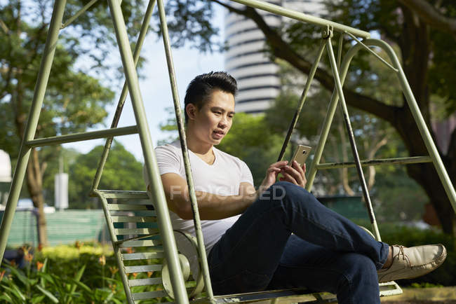 Young handsome male businessman using smartphone on swing — Stock Photo