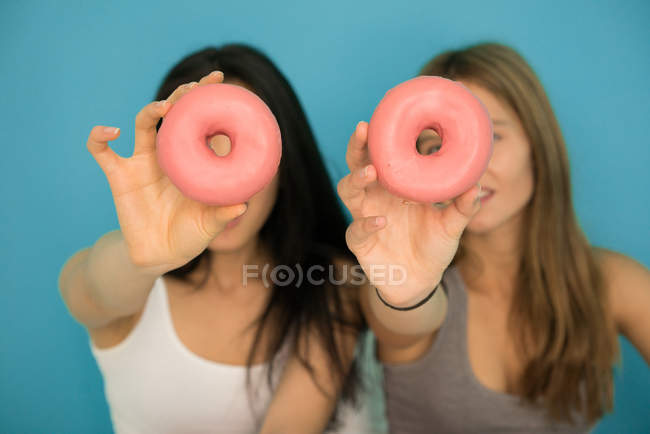 Two young women having fun with donuts — Stock Photo