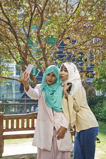 Belles femmes dans un tudung prendre des selfies au parc à Singapour — Photo de stock
